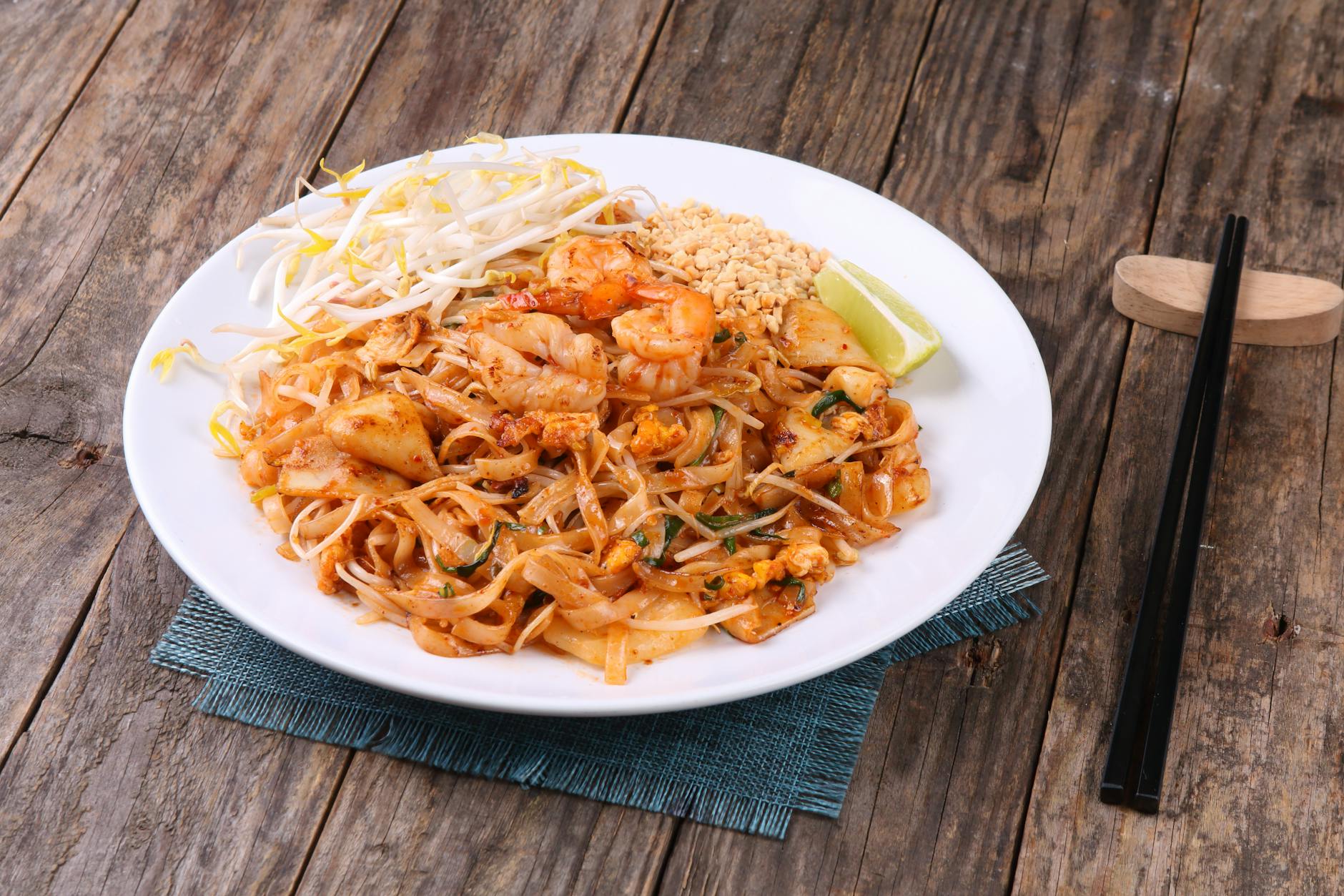 Delicious Pad Thai with shrimp, peanuts, lime, and bean sprouts on a rustic wooden table.